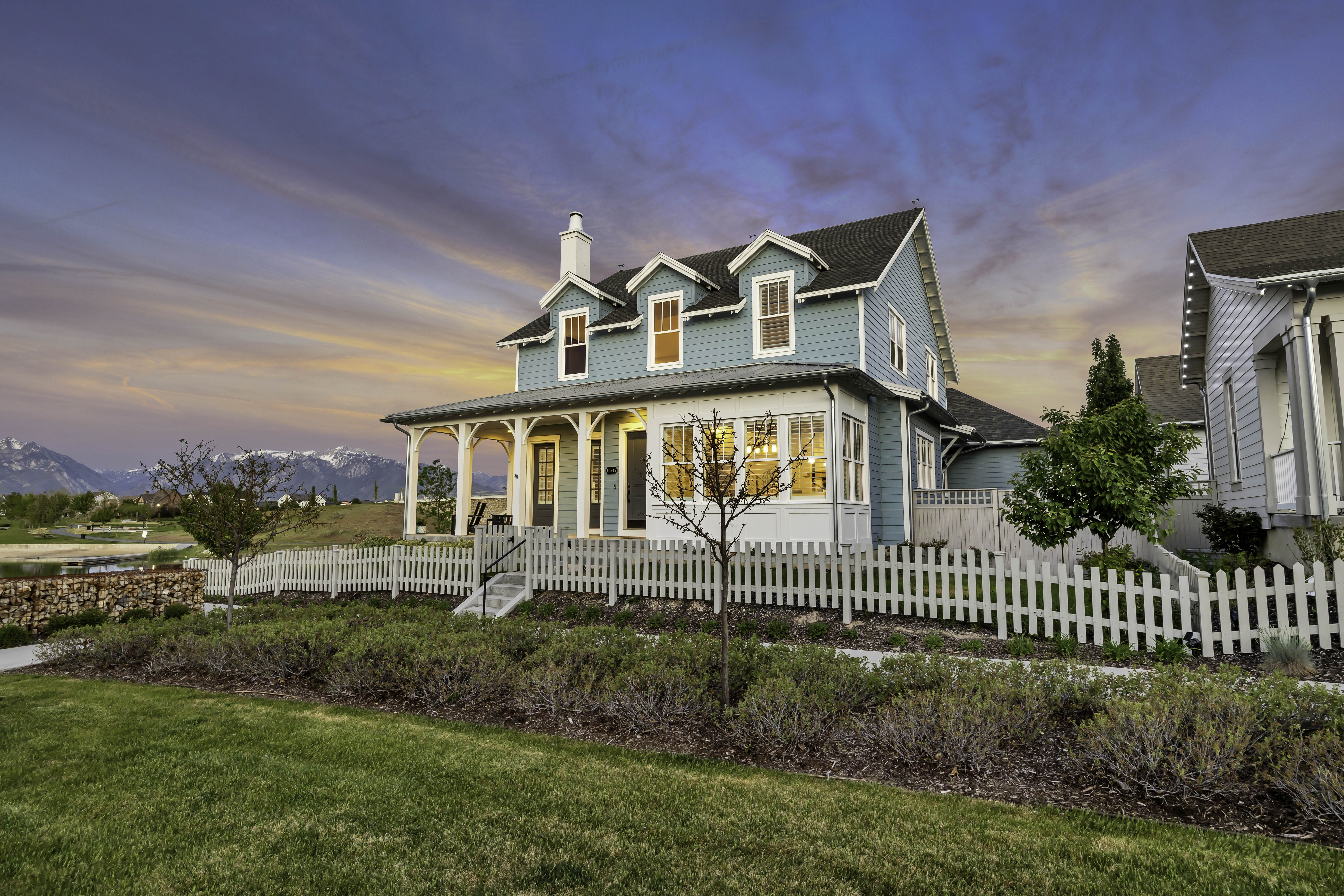 Light blue siding exterior featuring a white picket fence, covered front porch, dormer windows, and a manicured lawn