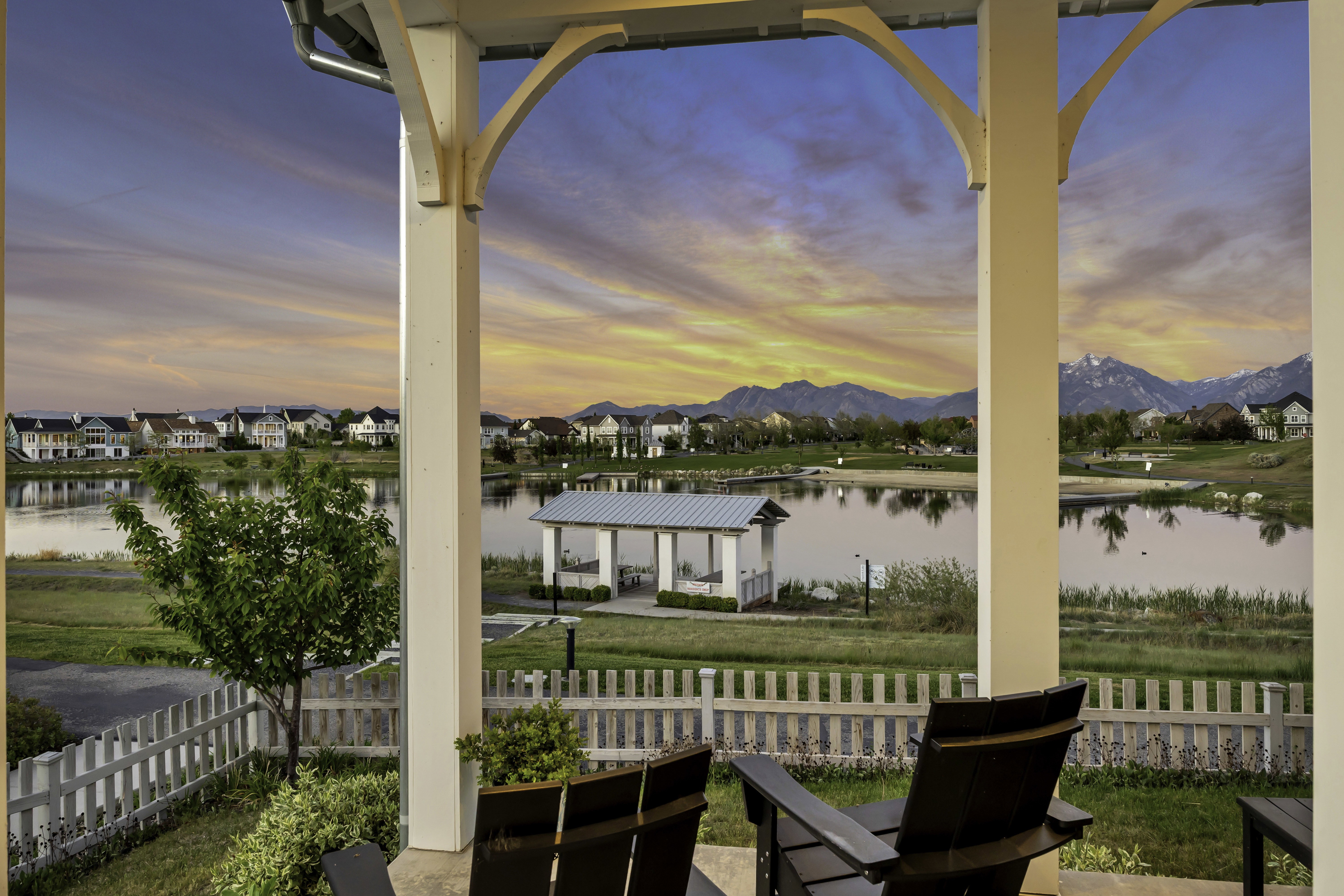 Covered outdoor patio with decorative corbels, white picket fence, and a landscaped yard