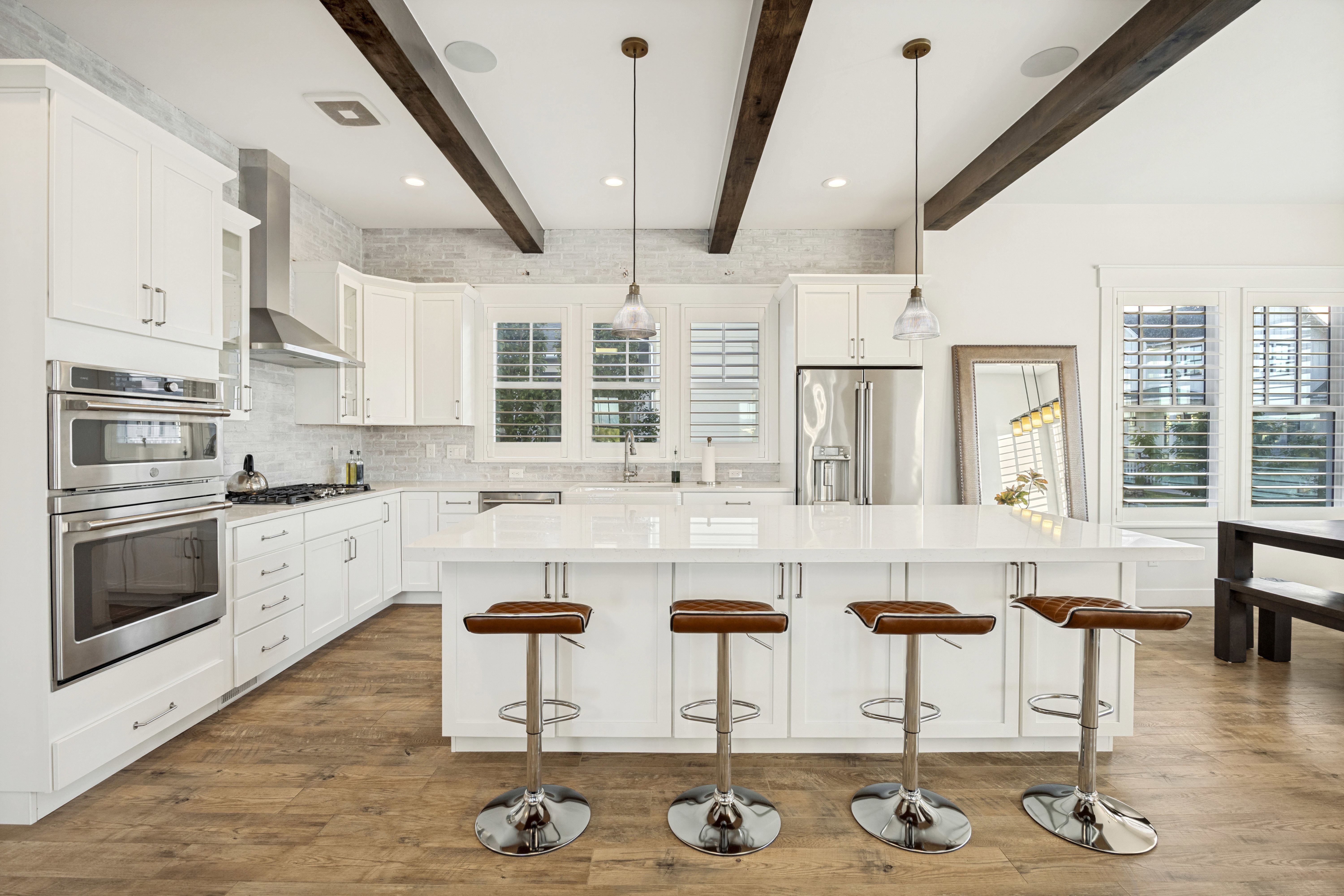 Kitchen featuring a large central island with seating, white shaker cabinetry, stainless steel appliances, and wood-finish flooring