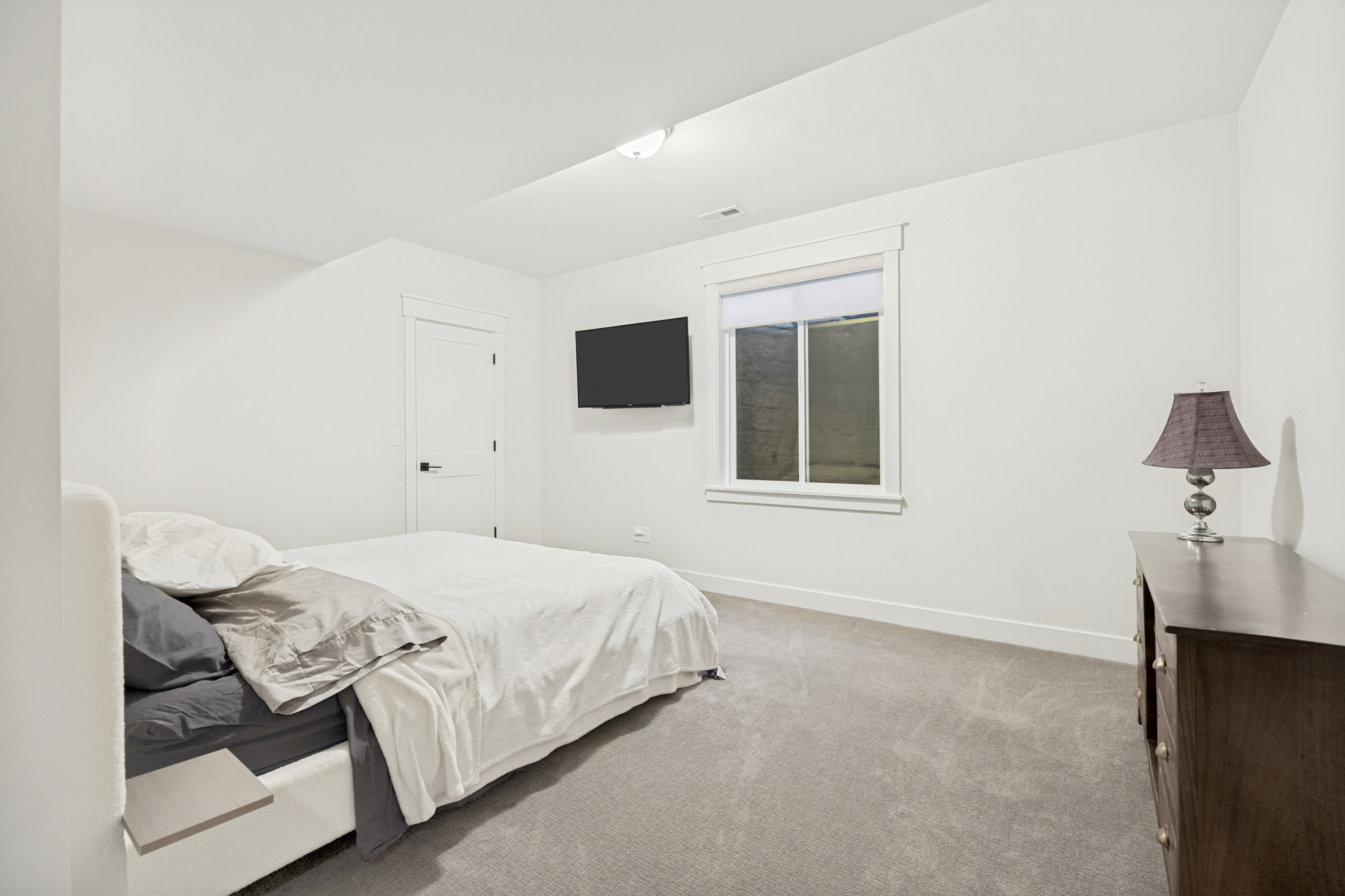 Bedroom featuring light gray carpeting, crisp white walls, a white trim window, a white interior door with black hardware, and a ceiling-mounted light fixture