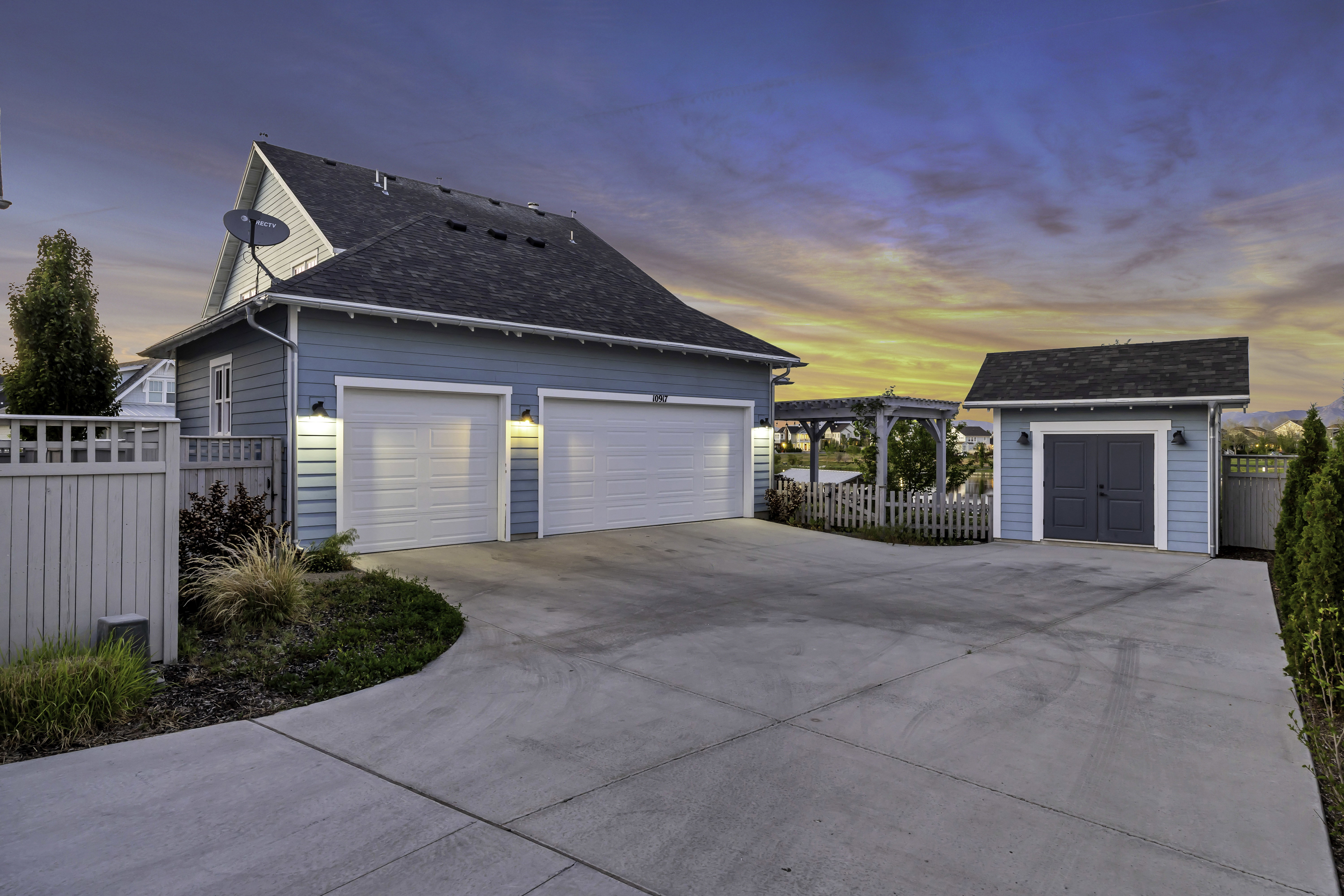 Property exterior featuring a two-car garage, separate storage shed, concrete driveway, and pergola