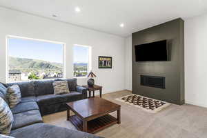 Living area featuring large picture windows, recessed lighting, a modern fireplace, a wall-mounted flat-screen television, and neutral carpet flooring