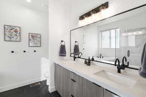 Dual vanity featuring wood-finish cabinetry, white countertops, and matte black fixtures