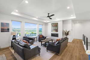 Open-concept living area featuring a tray ceiling with recessed lighting, an integrated ceiling fan, and large windows offering a scenic mountain and city landscape