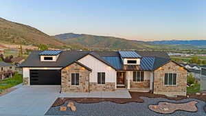 Contemporary exterior featuring stone accents, white vertical siding, and a dark shingle roof with two prominent metal dormers