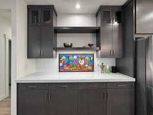 Kitchenette featuring dark wood-finish cabinetry, light-toned countertops, and a white tile backsplash