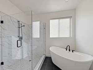 Freestanding soaking tub with matte black fixtures, alongside a glass-enclosed shower featuring large format veined wall tiles and a rainfall showerhead