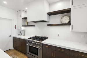 Contemporary kitchen featuring a stainless steel range with a ventilation hood, white subway tile backsplash, white countertops, and both white and wood-finish cabinetry