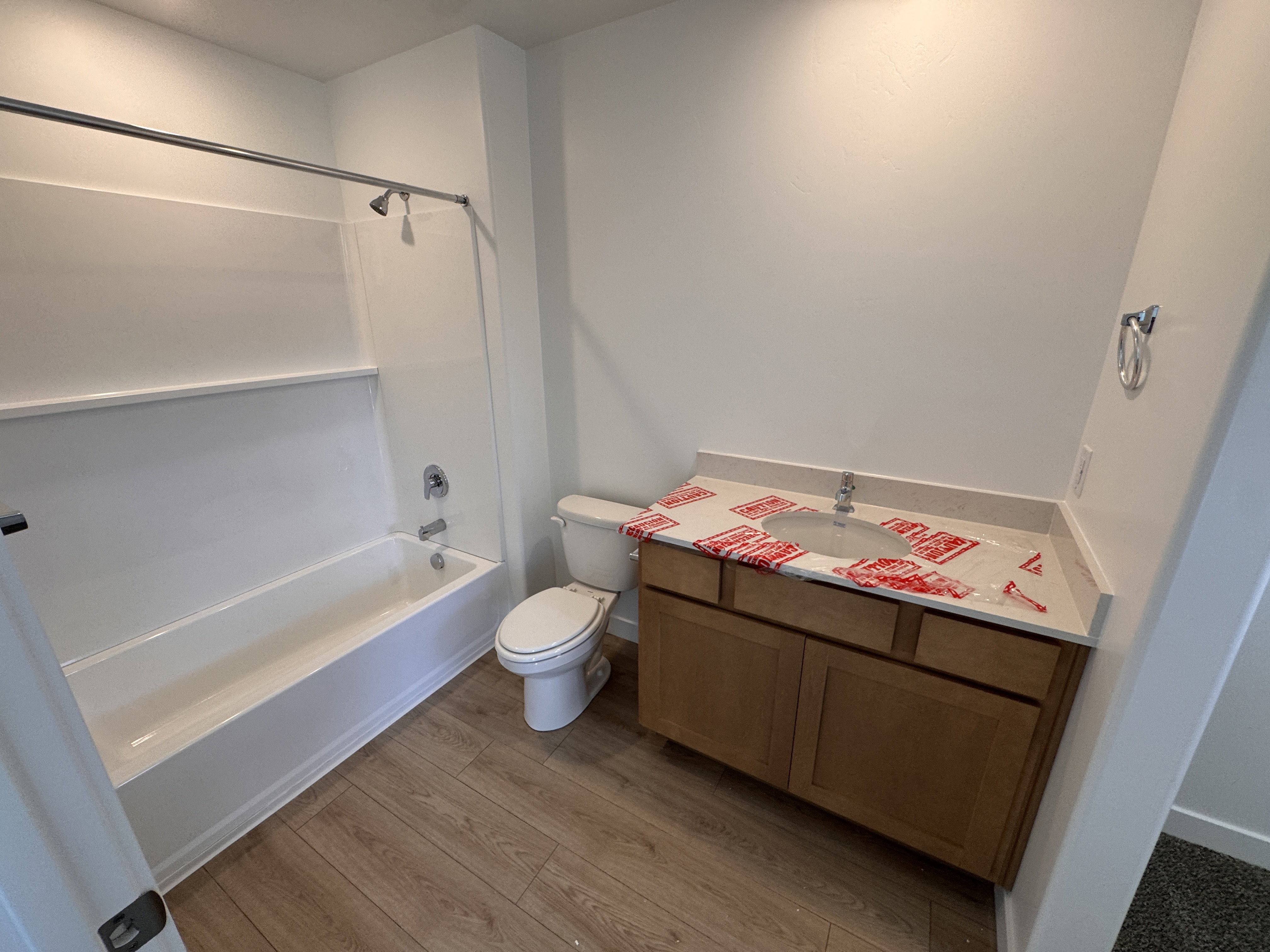 Full bathroom featuring a white tub and shower combination with chrome fixtures, a wood-finish vanity with a single sink and light-toned countertop, and wood-finish flooring