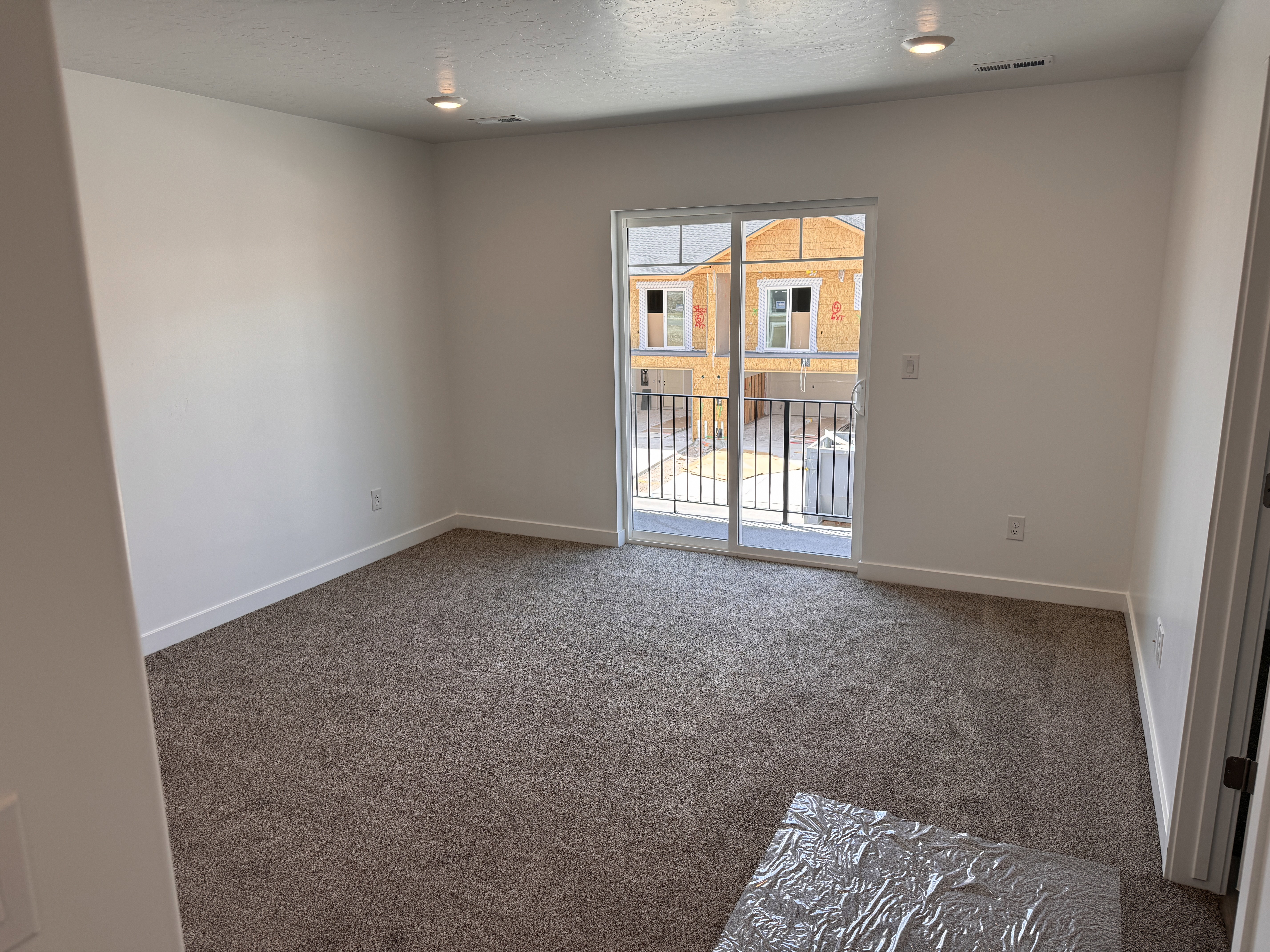 Spacious room featuring neutral carpeting, white baseboards, recessed ceiling lighting, and a sliding glass door providing balcony access