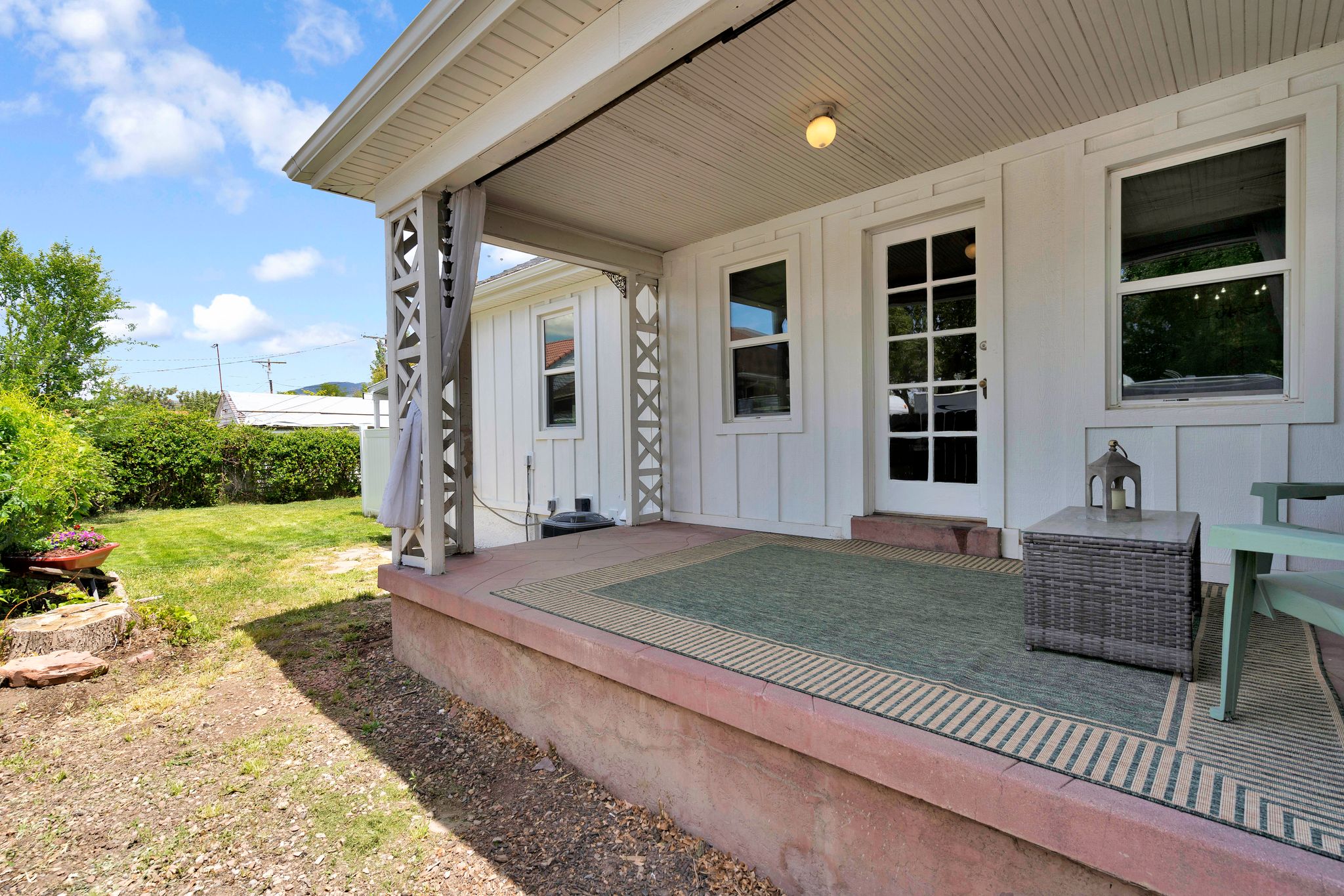 Covered concrete porch with decorative wood columns, white vertical siding, and a multi-pane glass door
