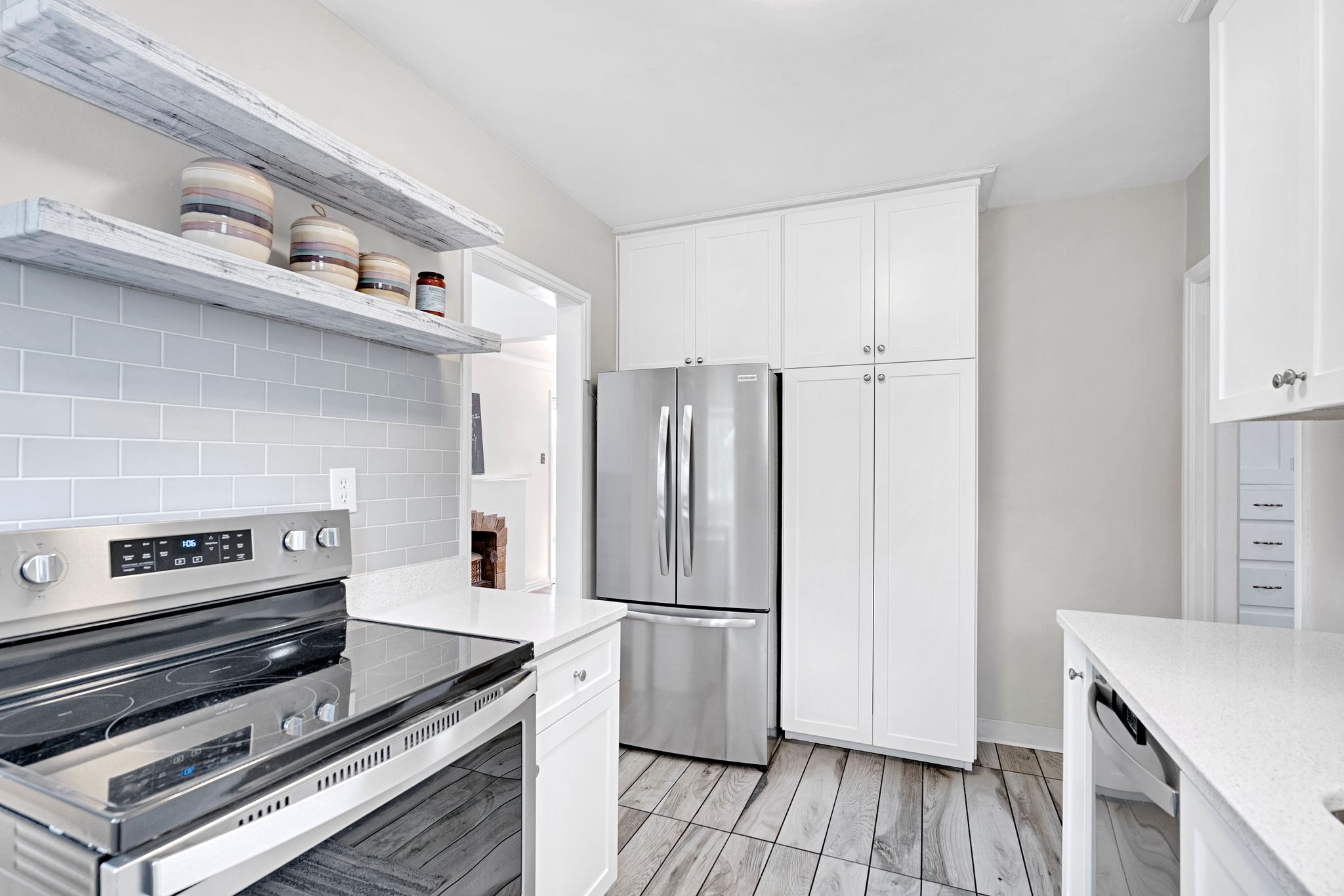 Modern kitchen featuring white shaker cabinetry, stainless steel appliances, light gray subway tile backsplash, white quartz countertops, and wood-finish tile flooring