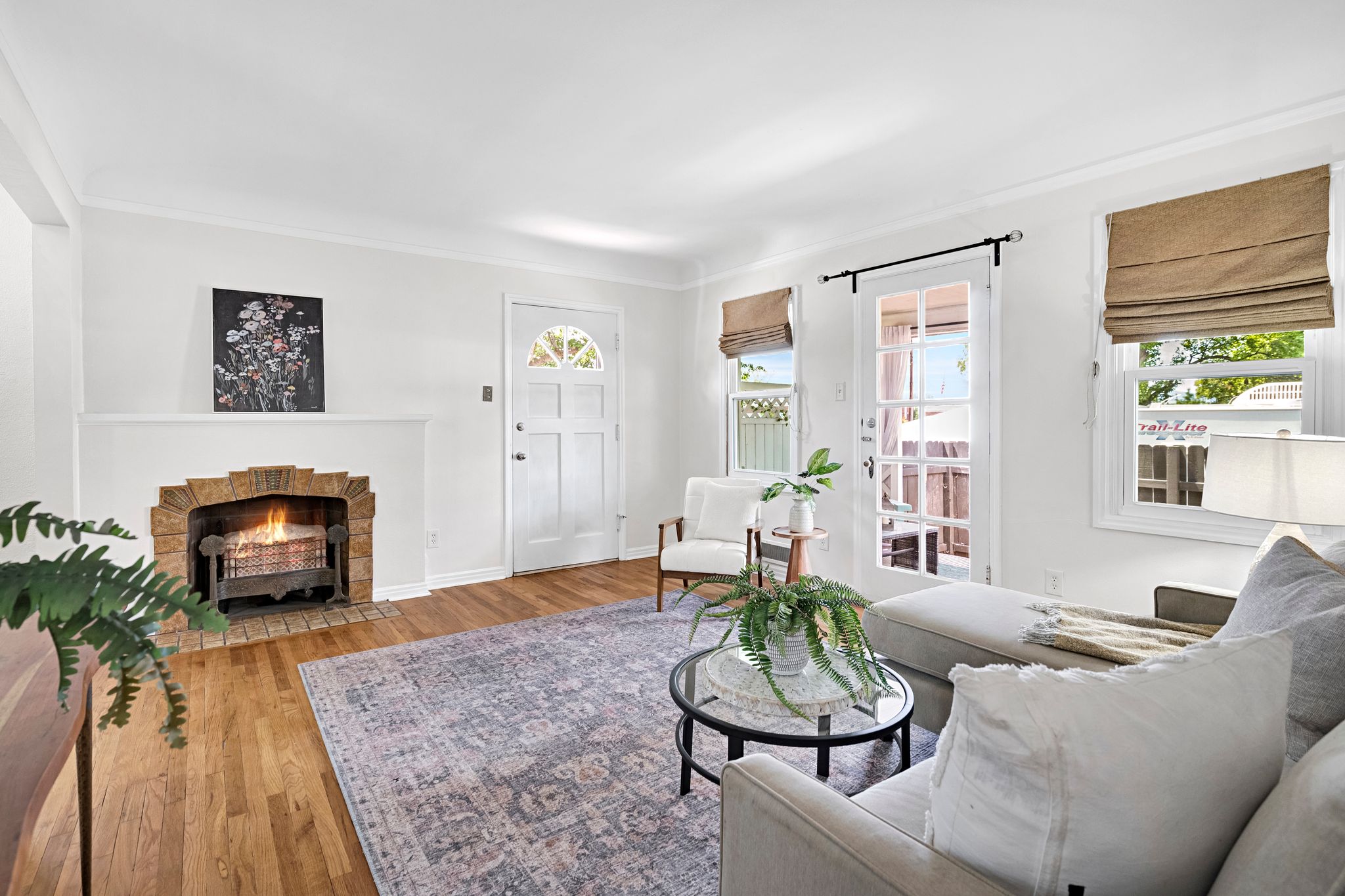 Living area featuring wood-finish flooring, a brick fireplace with a white mantel, and white walls