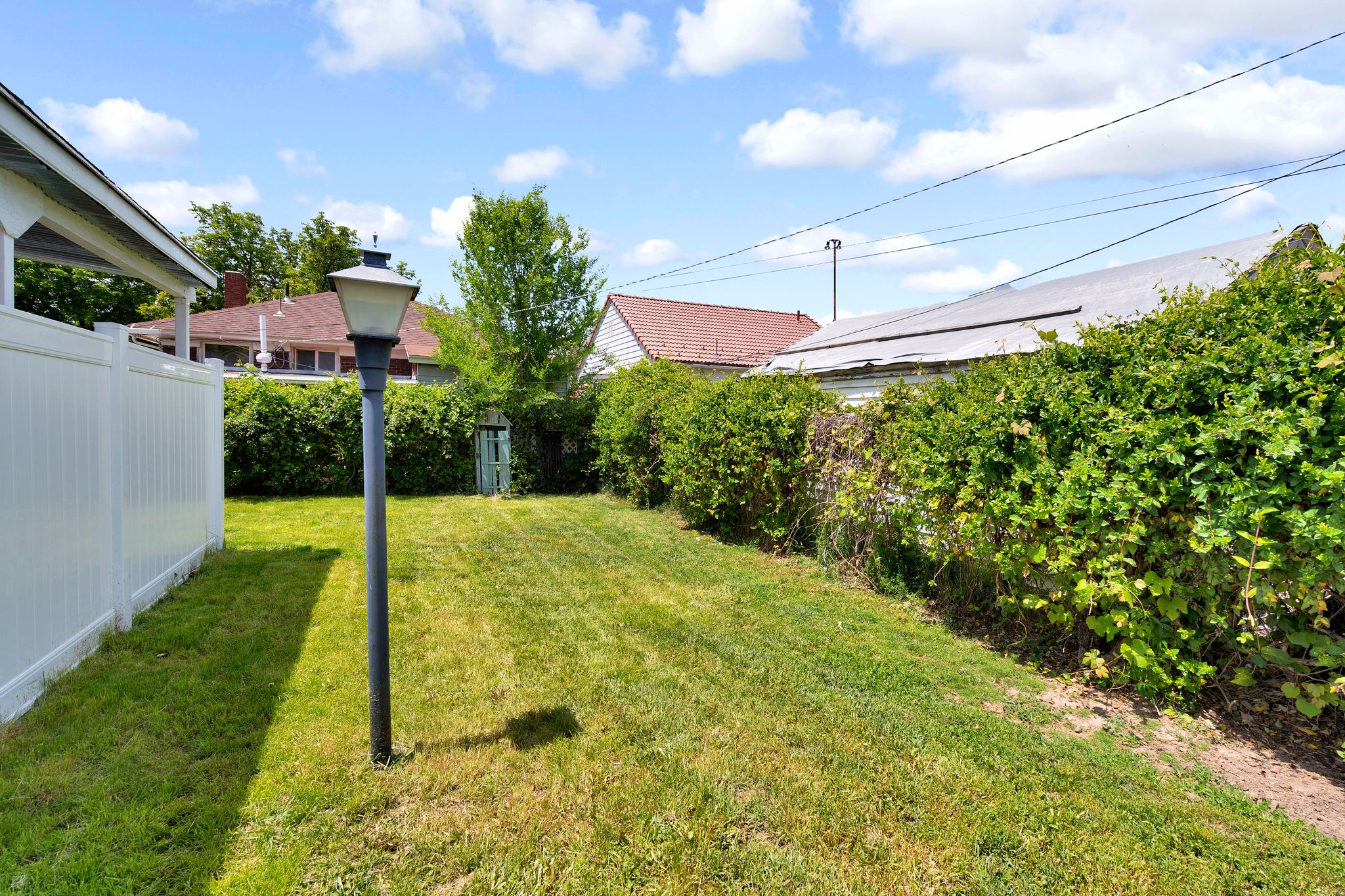 Expansive lawn area featuring a white privacy fence, mature perimeter hedging, and a traditional outdoor light fixture
