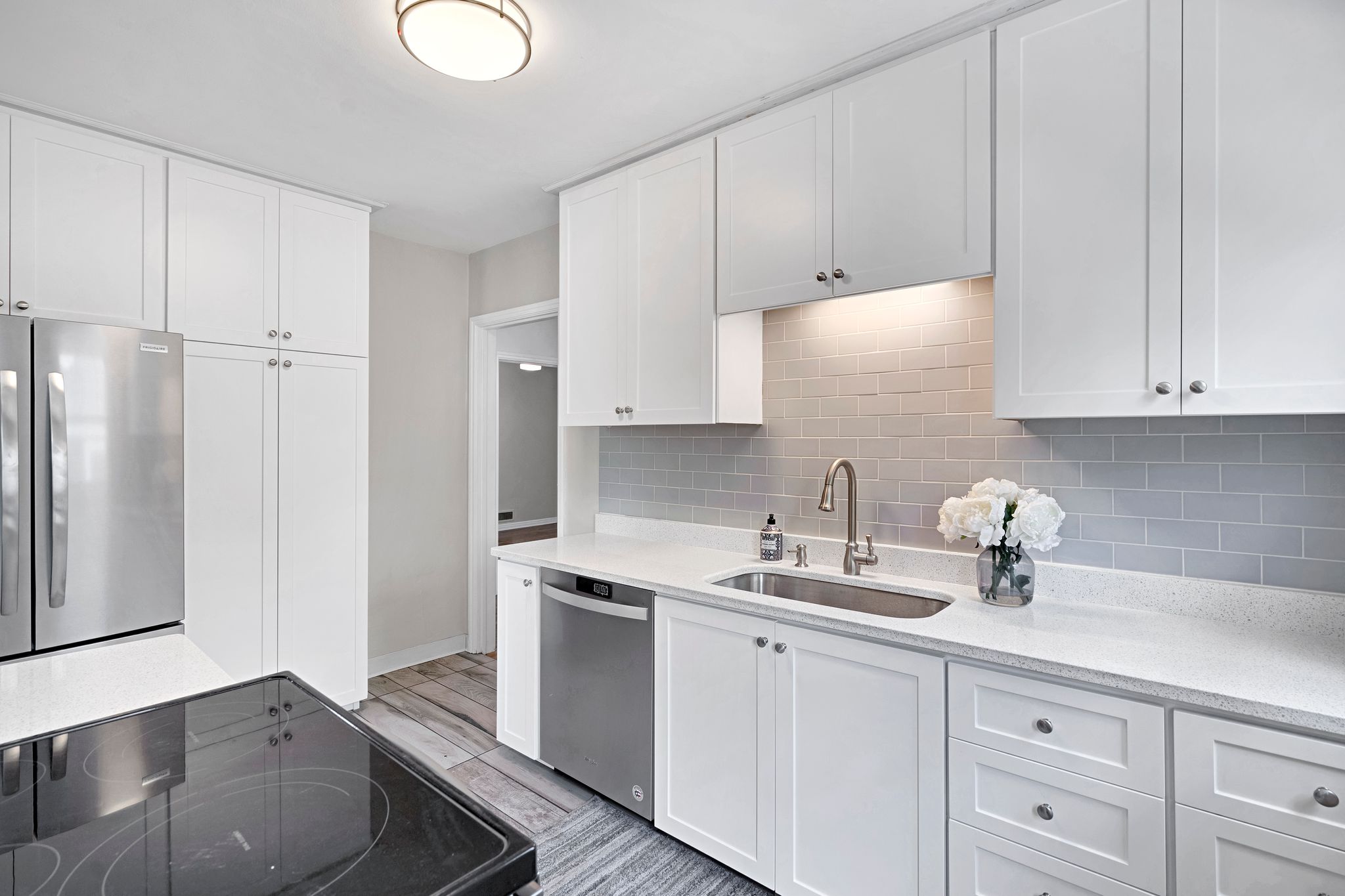 Kitchen featuring white shaker cabinetry, stainless steel appliances, light-toned countertops, subway tile backsplash, and wood-finish flooring