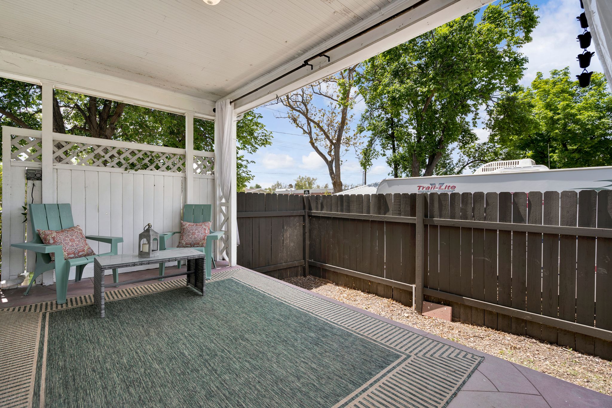 Covered patio featuring a white lattice privacy screen, durable wood-finish flooring, and a dark-toned privacy fence