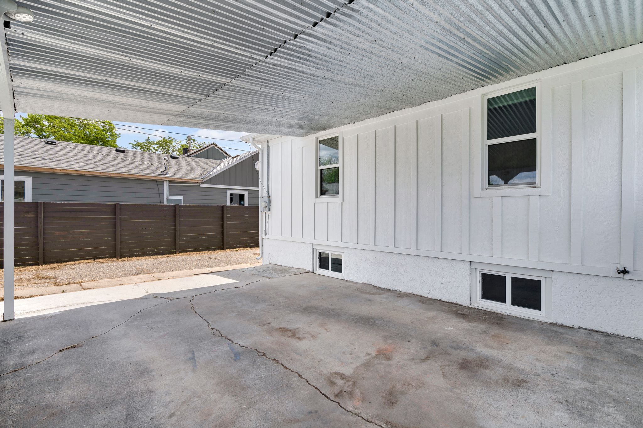 Covered carport featuring a corrugated metal ceiling, concrete surface, and white vertical panel siding