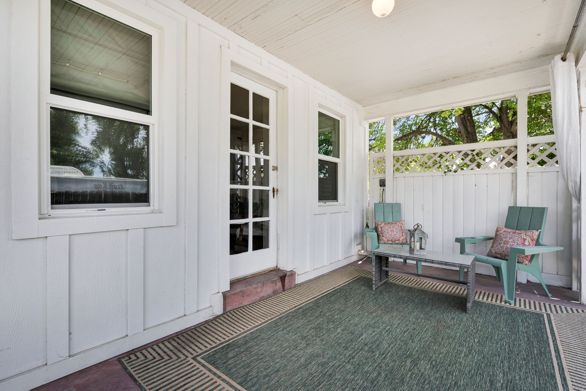 Covered porch featuring white vertical siding, a grid-patterned privacy screen, and a paneled glass door