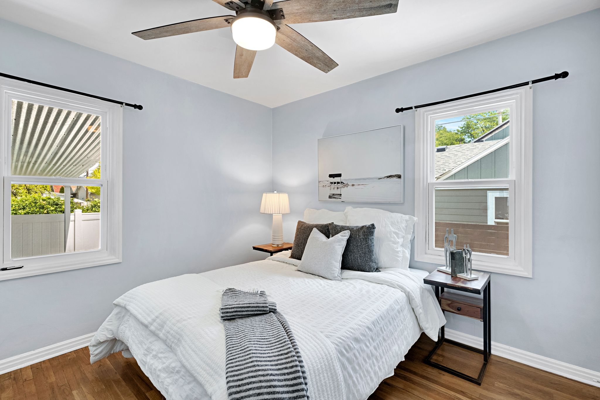 Bedroom featuring wood-finish flooring, two large windows, baseboard molding, a ceiling fan with integrated lighting, and light blue wall paint