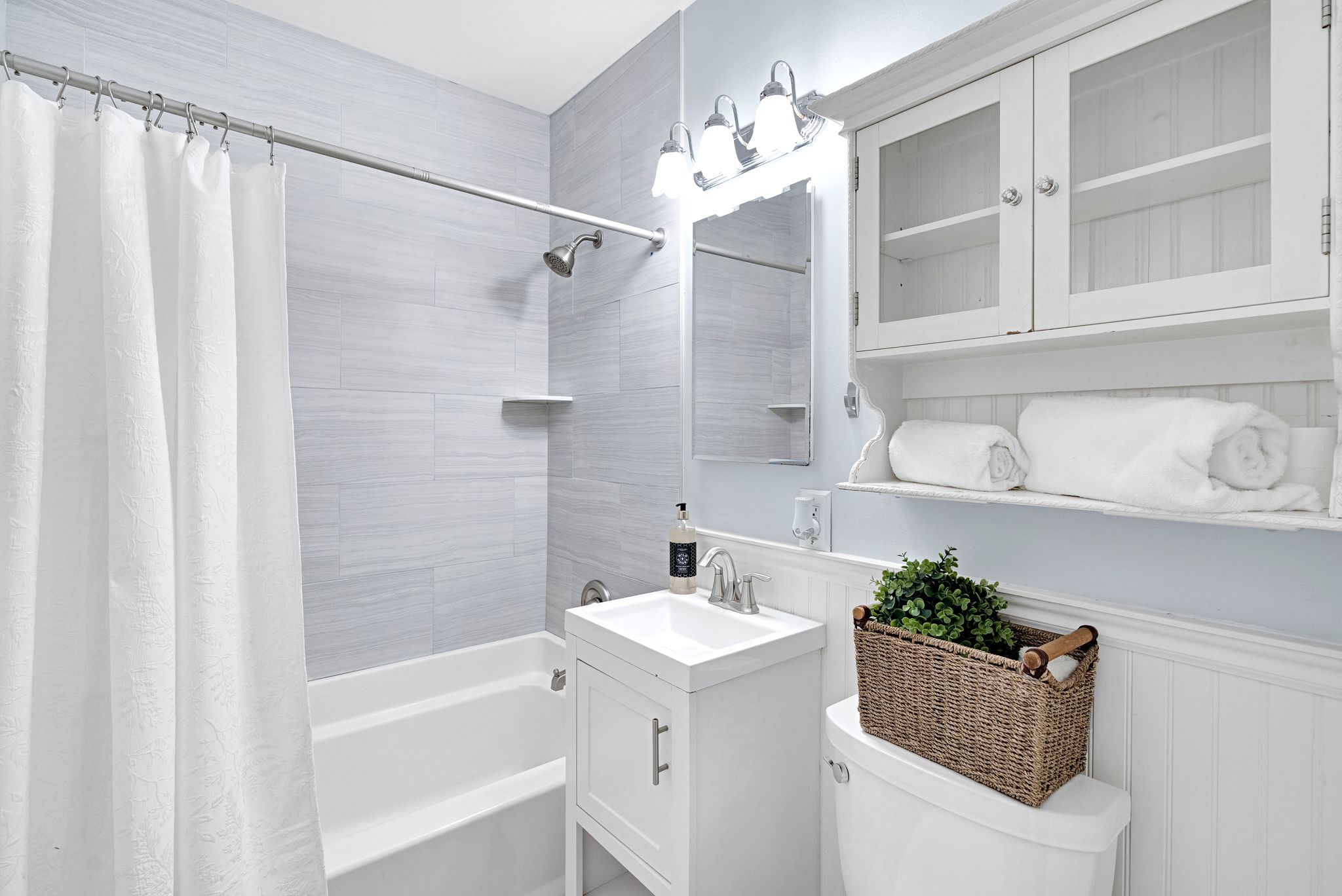 Bathroom featuring a white vanity with integrated sink, chrome faucet, and a shower-over-tub combination with light-toned tiled walls