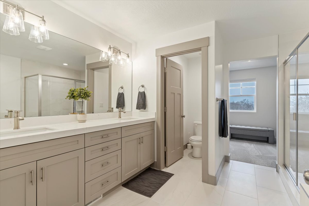 Spacious bathroom featuring a dual vanity with light-toned cabinetry and brushed nickel hardware, expansive mirror, and a glass-enclosed shower