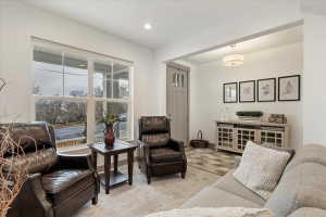 Bright living area featuring a large window with white trim, soft gray carpeting, a neutral wall color, a light wood-finish console cabinet, and a contemporary flush-mount ceiling light