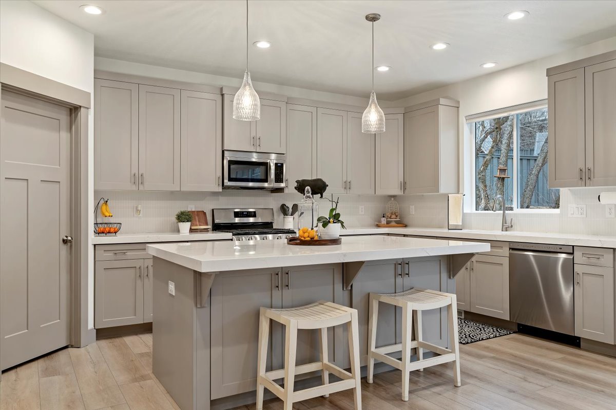 Contemporary kitchen featuring light gray cabinetry, stainless steel appliances, a center island with seating, pendant lighting, and wood-finish flooring