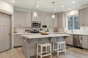 Contemporary kitchen featuring light gray cabinetry, stainless steel appliances, a center island with seating, pendant lighting, and wood-finish flooring