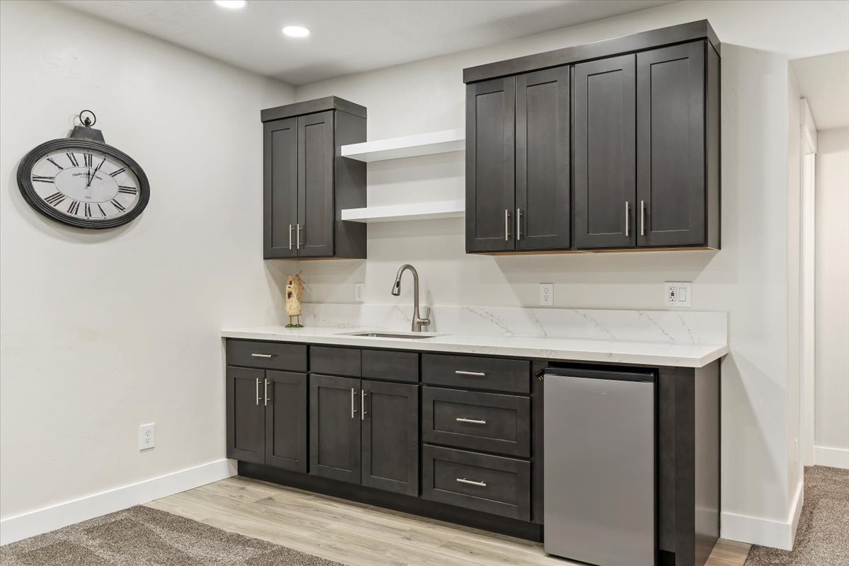 Built-in wet bar featuring dark cabinetry, a stainless steel sink, a modern faucet, quartz countertops, and a compact refrigerator
