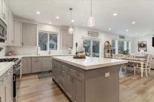 Contemporary kitchen featuring light gray shaker cabinetry, stainless steel appliances, a large island with a light-toned countertop, recessed lighting, and wood-finish flooring