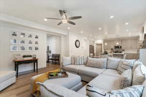 Open-concept living area featuring wood-finish flooring, a ceiling fan with integrated lighting, and recessed lighting throughout