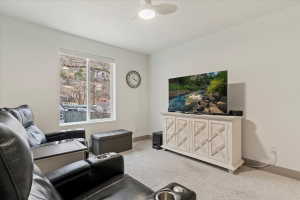 Carpeted interior space featuring a large window, white walls, and a ceiling fan