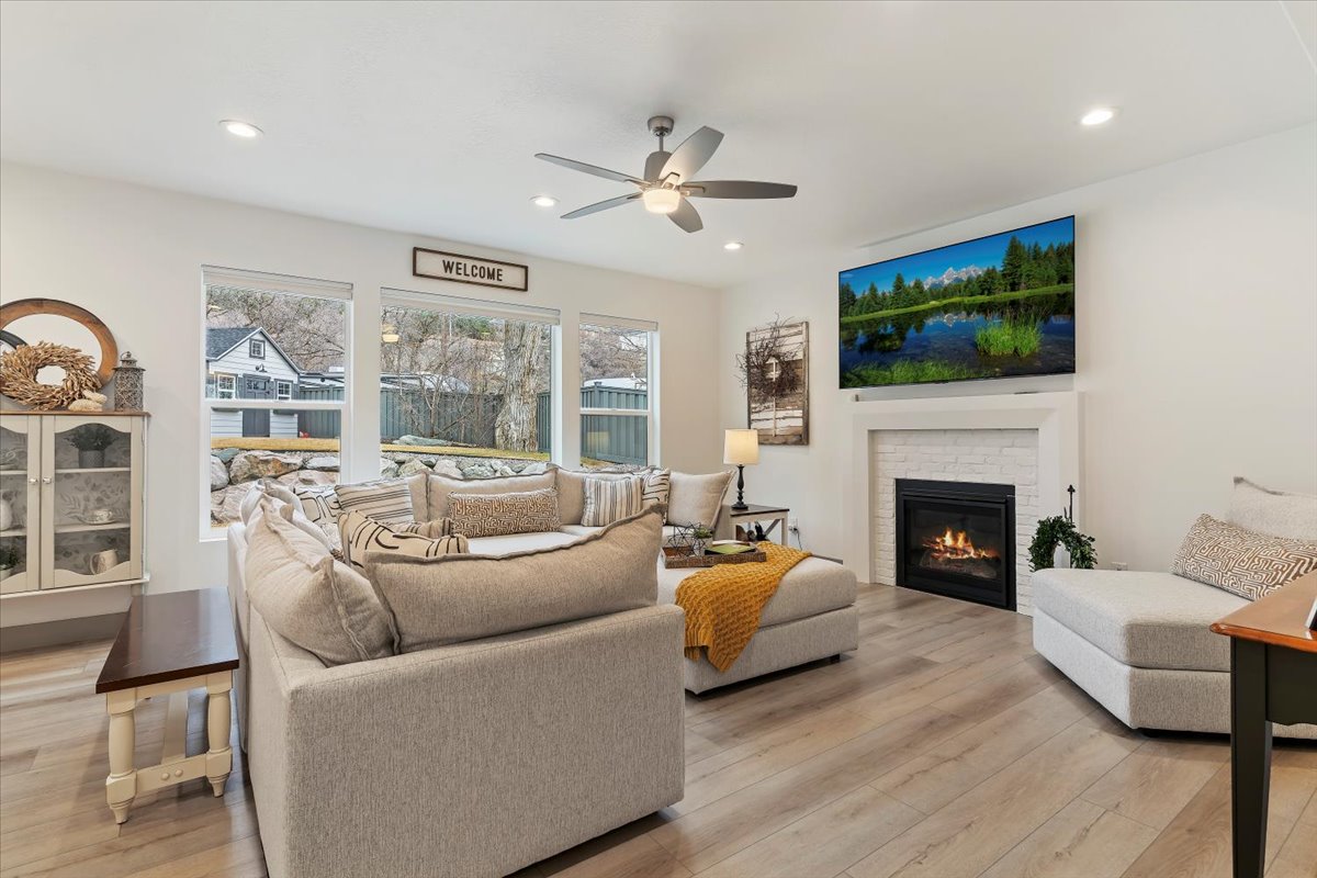 Living area featuring wide plank wood-finish flooring, a white brick fireplace with a substantial mantel, and recessed lighting