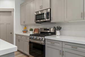 Contemporary kitchen featuring grey shaker-style cabinetry, stainless steel appliances including a range and over-the-range microwave, white countertops, and a white tile backsplash
