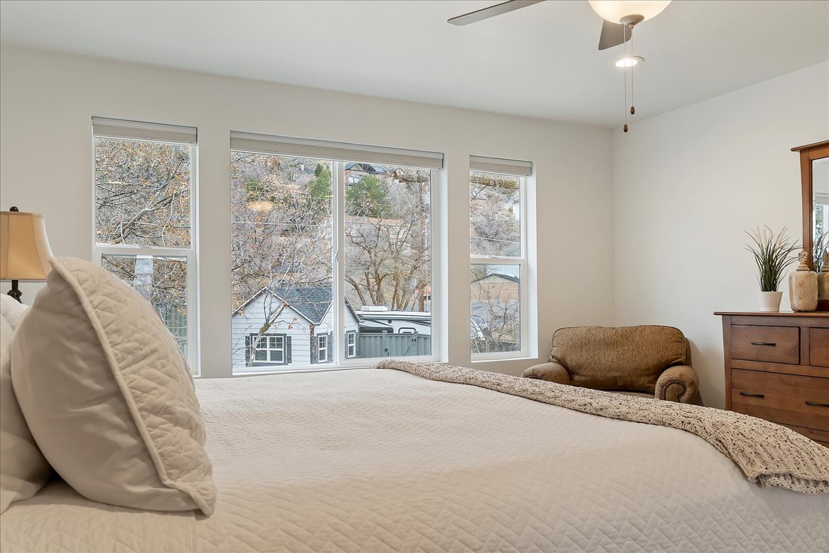 Bedroom featuring a wall of windows, overhead ceiling fan with lighting, white walls, and wood-finish dresser with an integrated mirror