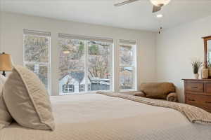 Bedroom featuring a wall of windows, overhead ceiling fan with lighting, white walls, and wood-finish dresser with an integrated mirror