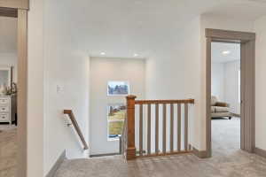 Carpeted hallway featuring a wood and painted baluster railing, recessed lighting, and a square window