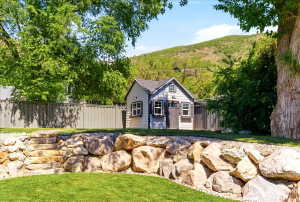 Landscaped backyard featuring a tiered rock retaining wall with stone steps, a manicured lawn, and a custom storage shed with board and batten siding