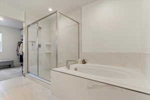 Spacious bathroom featuring a built-in soaking tub with deck-mounted fixtures, a glass-enclosed shower with tile surround and recessed shelving, and large format tile flooring