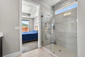 Glass-enclosed shower featuring light grey tile walls with a decorative accent band, a pebble-stone shower floor, and a transom window