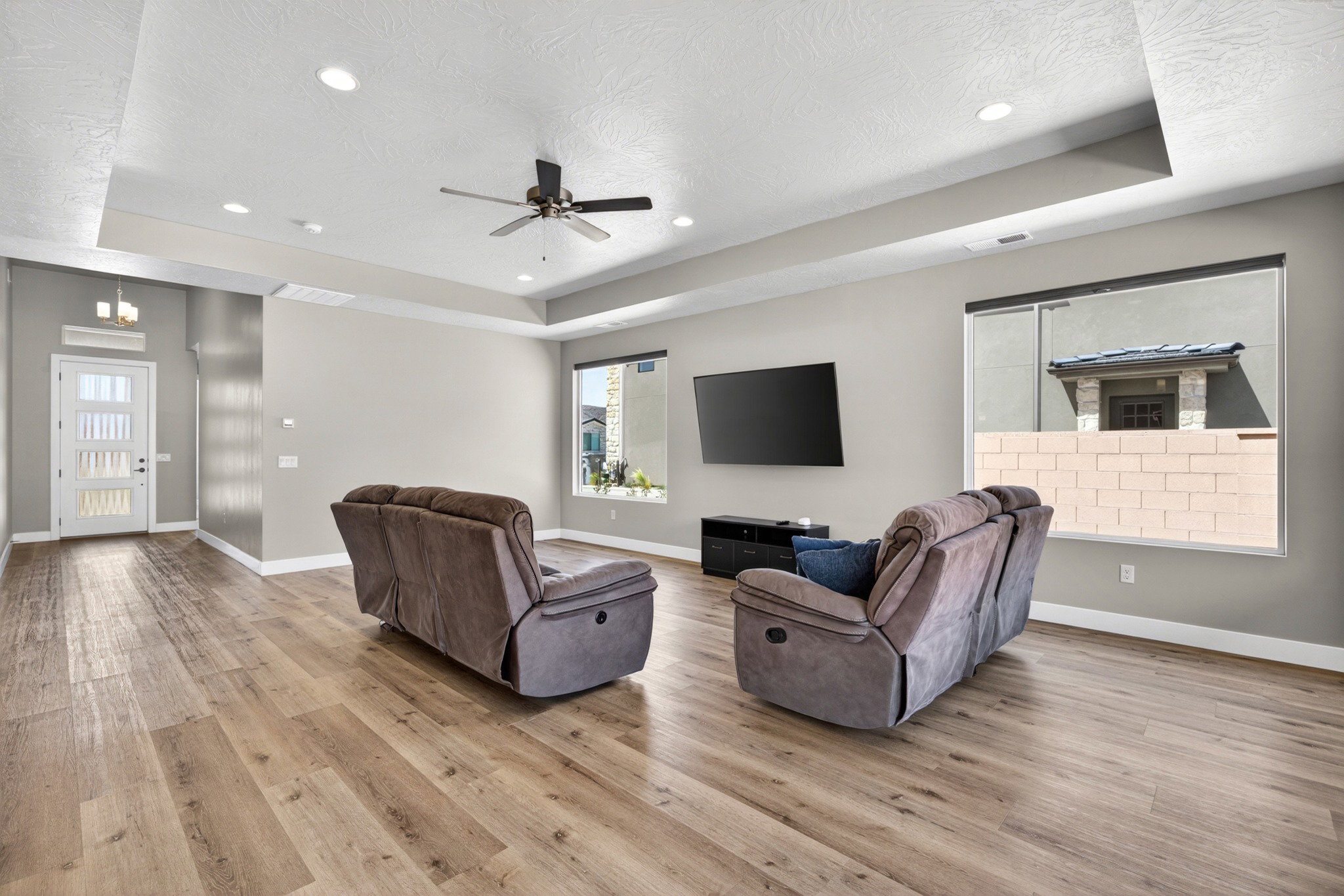 Expansive living area with wood-finish flooring, tray ceiling, recessed lighting, and a ceiling fan