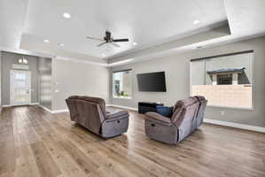Expansive living area with wood-finish flooring, tray ceiling, recessed lighting, and a ceiling fan