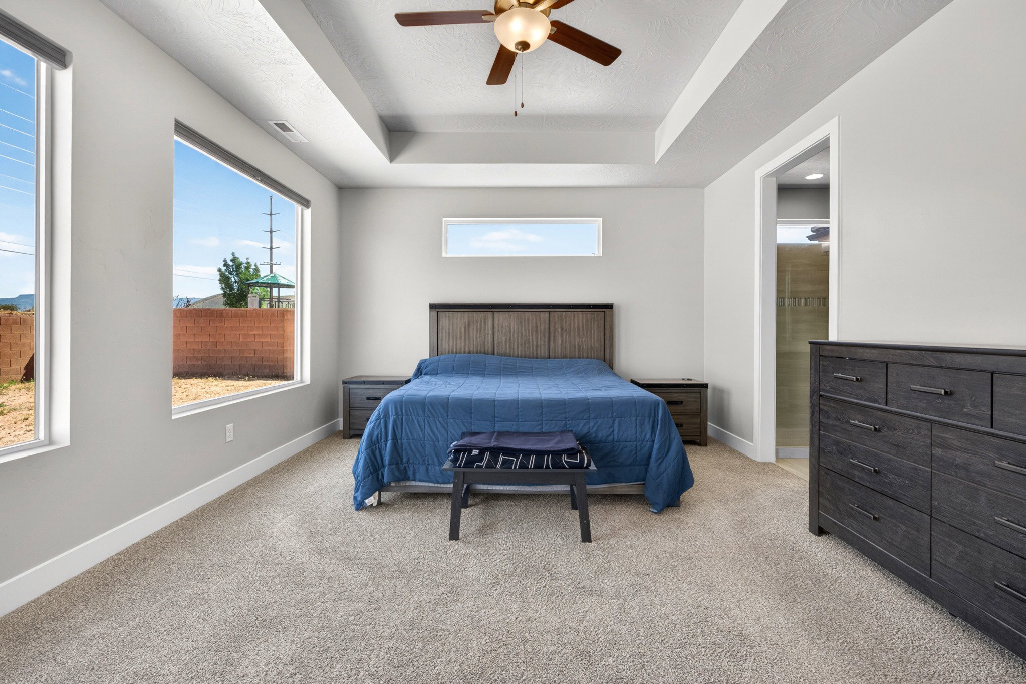 Bedroom featuring a tray ceiling with a ceiling fan, abundant natural light from large windows, light-toned carpeting, and light gray wall paint