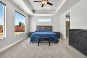 Bedroom featuring a tray ceiling with a ceiling fan, abundant natural light from large windows, light-toned carpeting, and light gray wall paint