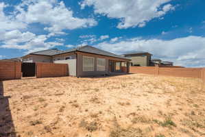 Expansive backyard space featuring a stucco exterior home with a covered patio, dark roof, and multiple large windows