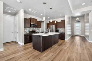 Open-concept kitchen featuring wood-finish flooring, dark wood cabinetry, a white countertop island with an undermount sink, and stainless steel appliances