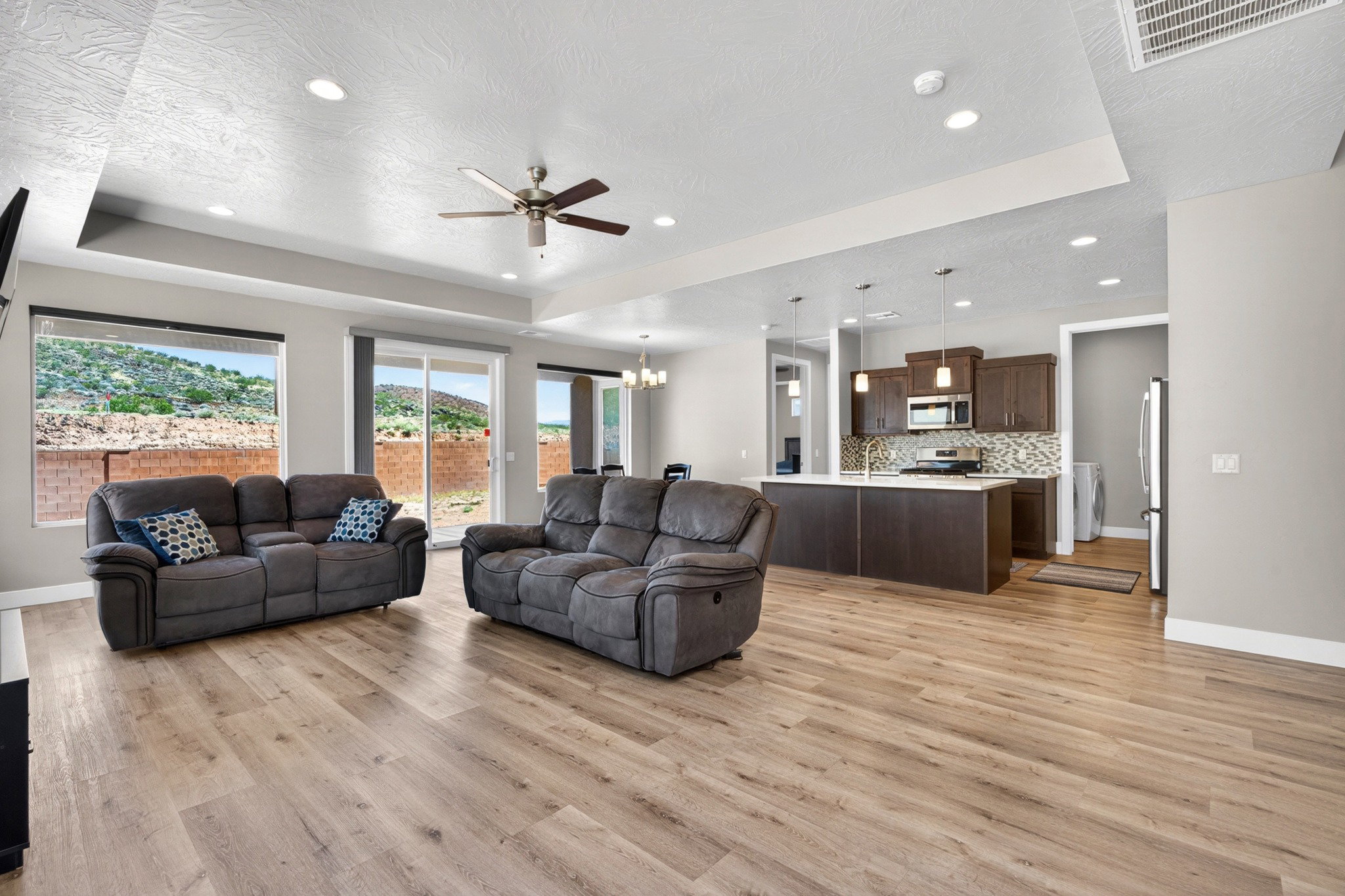 Open-concept living space featuring wood-finish flooring, recessed lighting, and a tray ceiling with a ceiling fan