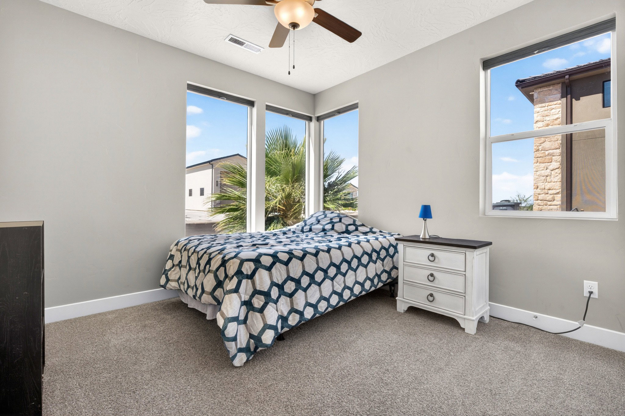 Carpeted room featuring multiple large windows, neutral gray walls, white baseboards, and a ceiling fan with integrated lighting