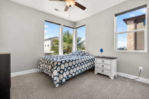 Carpeted room featuring multiple large windows, neutral gray walls, white baseboards, and a ceiling fan with integrated lighting
