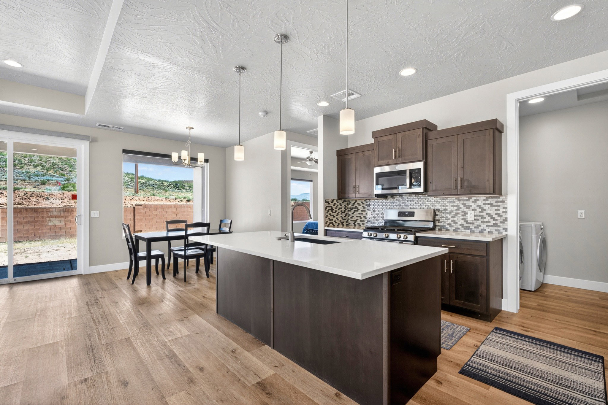 Contemporary kitchen featuring a spacious island with a white countertop, dark wood-finish cabinetry, and a mosaic tile backsplash